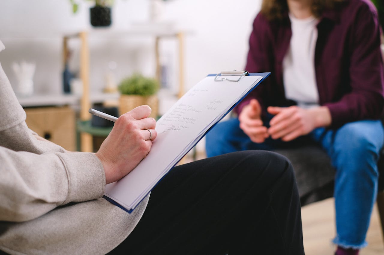about-us-img Close-up of a therapist writing notes on a clipboard while conversing with a patient.